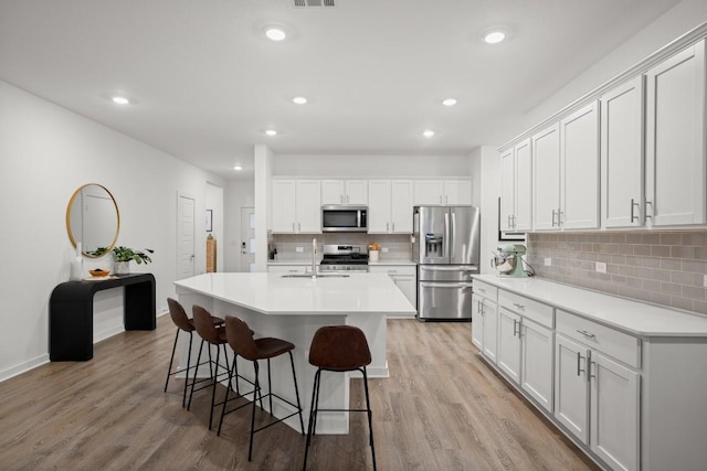 kitchen featuring stainless steel appliances, light hardwood / wood-style floors, a kitchen island with sink, and white cabinets