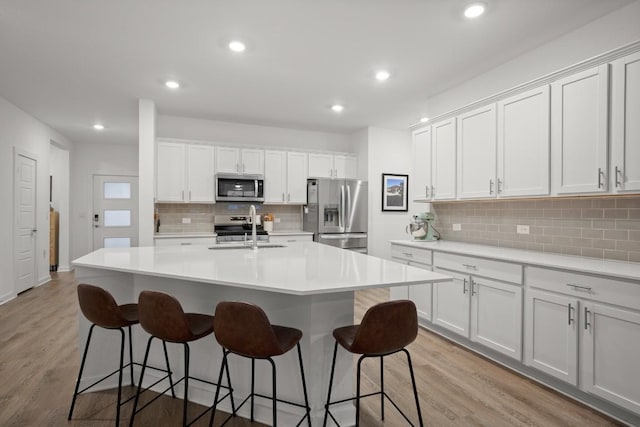 kitchen with sink, a center island with sink, appliances with stainless steel finishes, light hardwood / wood-style floors, and white cabinets