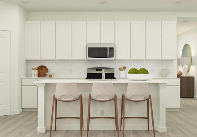 kitchen featuring white cabinetry, range, backsplash, and a center island with sink