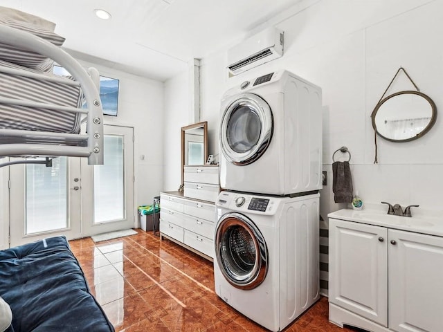 clothes washing area with stacked washing maching and dryer, a wall mounted air conditioner, sink, cabinets, and dark tile patterned floors