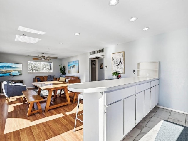 kitchen with a breakfast bar, ceiling fan, light hardwood / wood-style floors, white cabinets, and kitchen peninsula