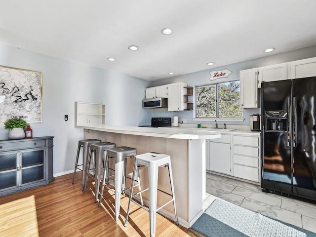 kitchen featuring white cabinetry, a kitchen bar, kitchen peninsula, and black appliances