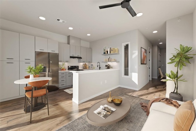 kitchen with gray cabinetry, range, kitchen peninsula, stainless steel refrigerator with ice dispenser, and light wood-type flooring