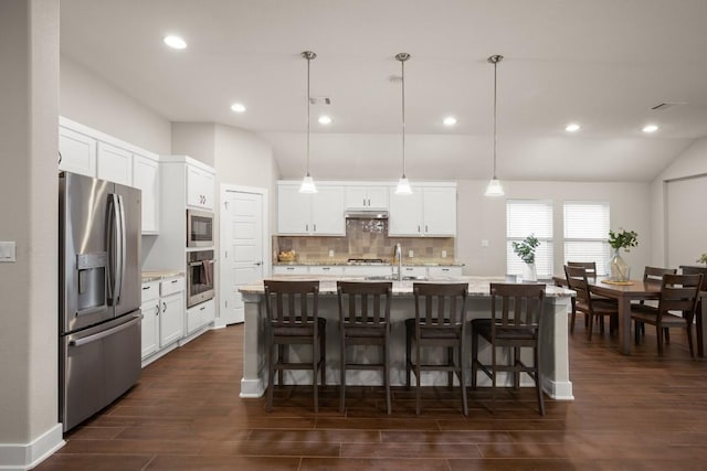 kitchen with stainless steel appliances, a center island with sink, pendant lighting, and white cabinets