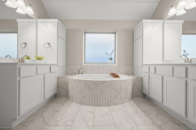 bathroom featuring vanity, vaulted ceiling, and tiled tub