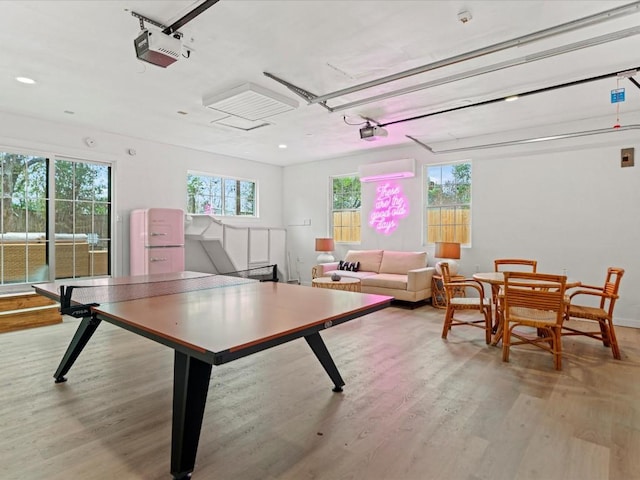 rec room with a healthy amount of sunlight, a wall mounted AC, and light hardwood / wood-style flooring