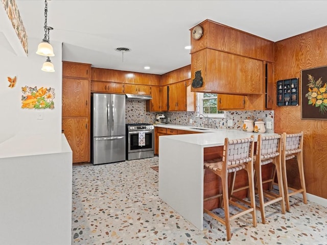 kitchen with pendant lighting, a breakfast bar, appliances with stainless steel finishes, tasteful backsplash, and kitchen peninsula