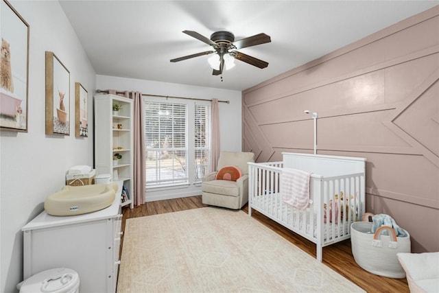 bedroom featuring a nursery area, ceiling fan, and wood-type flooring