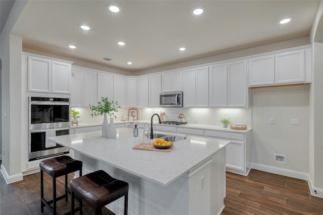 kitchen featuring white cabinetry, sink, light stone counters, stainless steel appliances, and a center island with sink