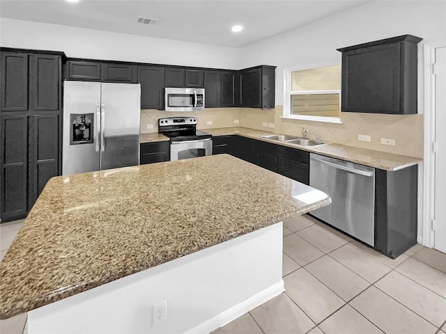 kitchen featuring stainless steel appliances, light stone countertops, a center island, and sink