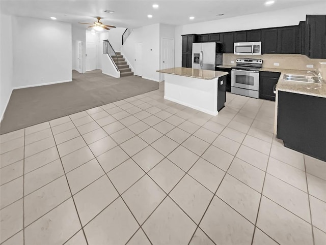 kitchen with a kitchen island, appliances with stainless steel finishes, sink, light stone countertops, and light carpet