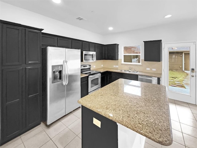 kitchen featuring light tile patterned flooring, sink, a center island, stainless steel appliances, and light stone countertops