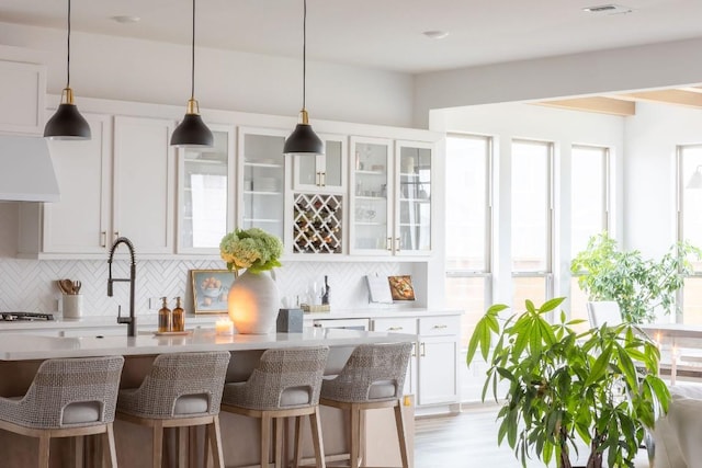 bar with pendant lighting, white cabinetry, tasteful backsplash, custom range hood, and stainless steel gas stovetop