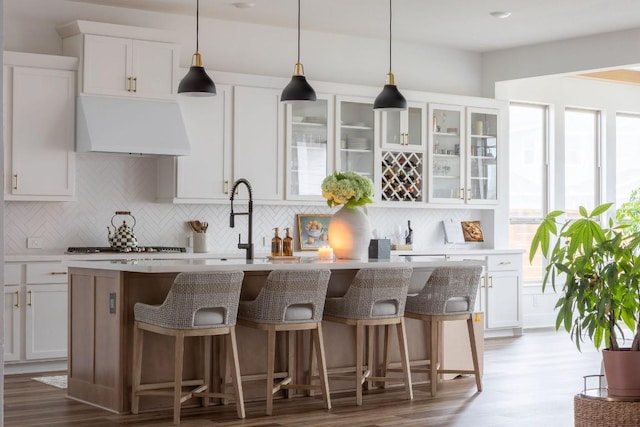 kitchen featuring white cabinetry, an island with sink, exhaust hood, and decorative light fixtures