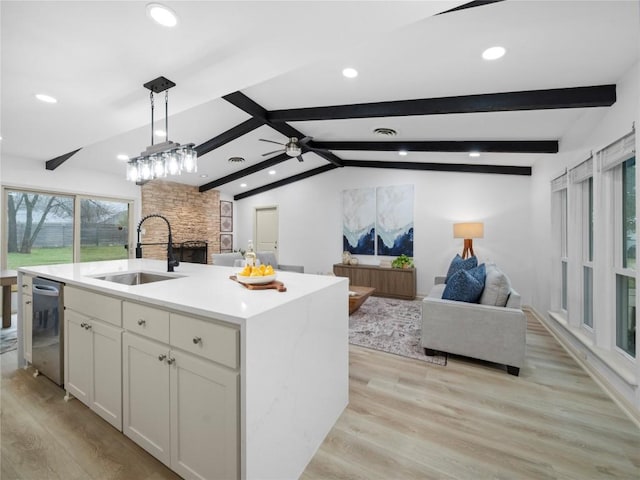 kitchen featuring decorative light fixtures, dishwasher, white cabinetry, sink, and a center island with sink