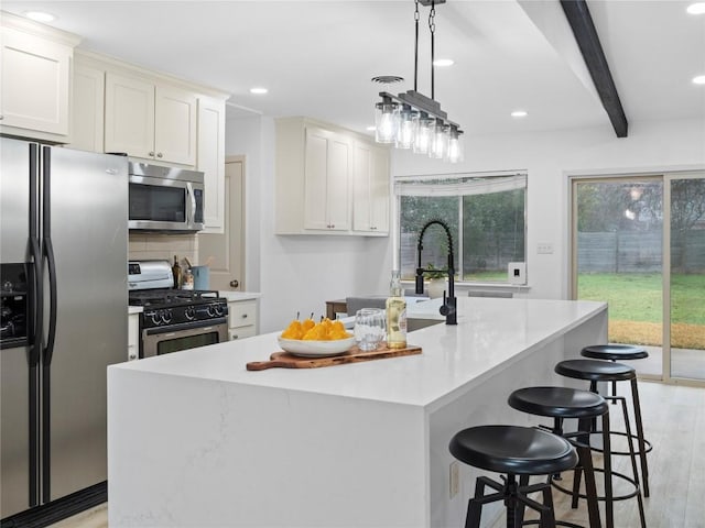 kitchen with white cabinetry, stainless steel appliances, an island with sink, and hanging light fixtures