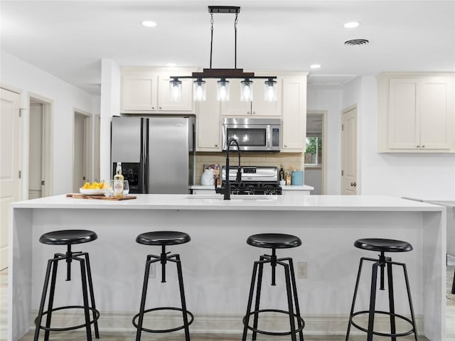 kitchen featuring hanging light fixtures, white cabinetry, appliances with stainless steel finishes, and a kitchen bar