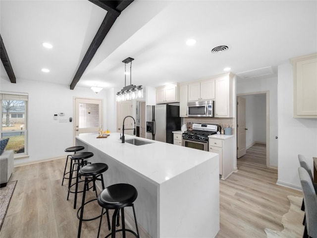 kitchen with appliances with stainless steel finishes, an island with sink, sink, white cabinets, and hanging light fixtures