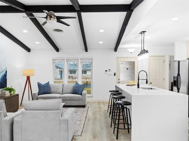 living room featuring sink, light hardwood / wood-style flooring, beamed ceiling, and ceiling fan