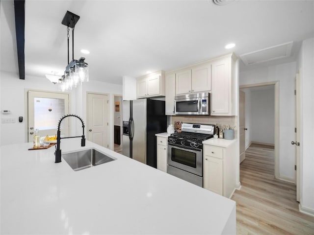 kitchen featuring sink, stainless steel appliances, light hardwood / wood-style floors, white cabinets, and decorative light fixtures