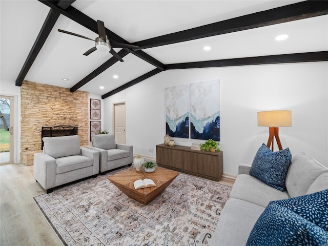 living room with ceiling fan, a stone fireplace, light hardwood / wood-style floors, and vaulted ceiling with beams