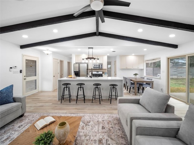 living room featuring sink, vaulted ceiling with beams, ceiling fan with notable chandelier, and light wood-type flooring