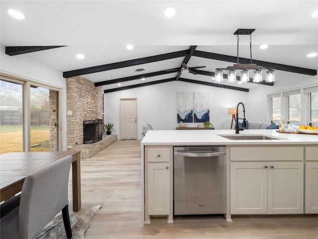 kitchen with a stone fireplace, pendant lighting, dishwasher, sink, and vaulted ceiling with beams