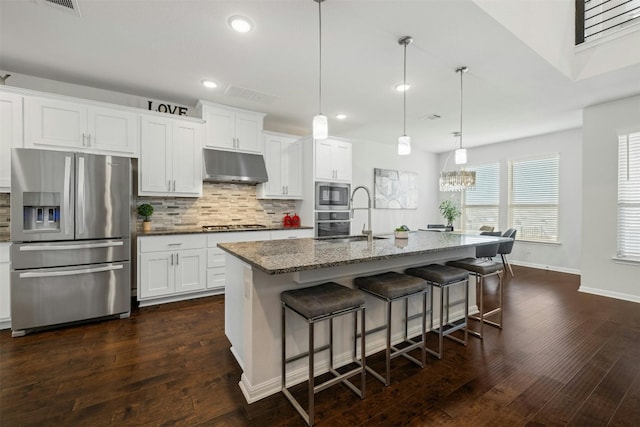 kitchen with pendant lighting, stainless steel appliances, a kitchen island with sink, and white cabinets