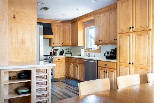 kitchen with wall chimney exhaust hood, sink, tasteful backsplash, light hardwood / wood-style flooring, and appliances with stainless steel finishes