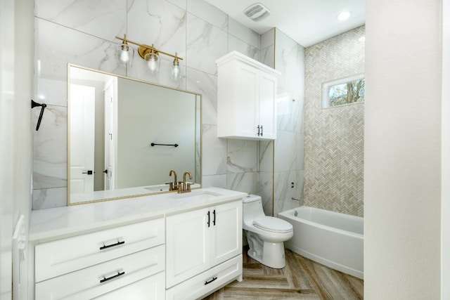 full bathroom with tiled shower / bath, tile walls, hardwood / wood-style flooring, vanity, and toilet