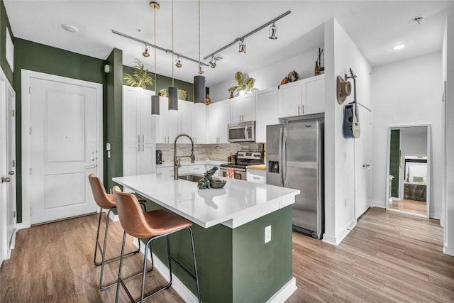 kitchen with sink, pendant lighting, stainless steel appliances, a kitchen island with sink, and white cabinets