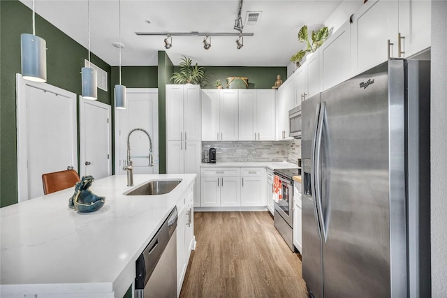 kitchen featuring appliances with stainless steel finishes, decorative light fixtures, white cabinetry, sink, and light stone countertops