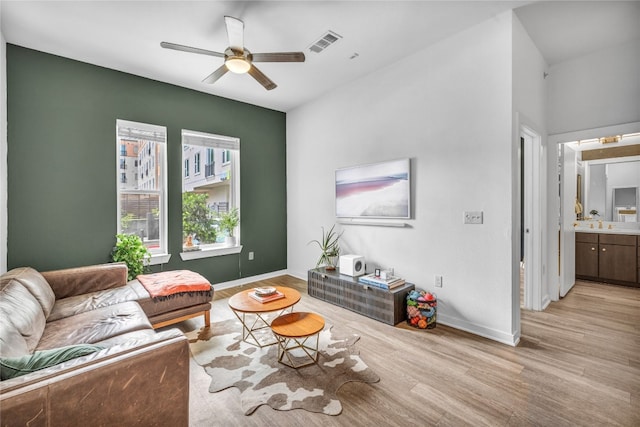 living room featuring light wood-type flooring, visible vents, baseboards, and a ceiling fan