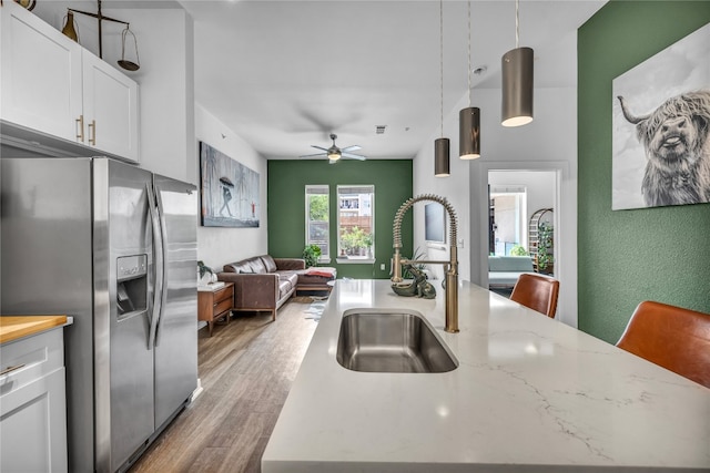 kitchen with sink, stainless steel refrigerator with ice dispenser, light stone counters, white cabinets, and decorative light fixtures