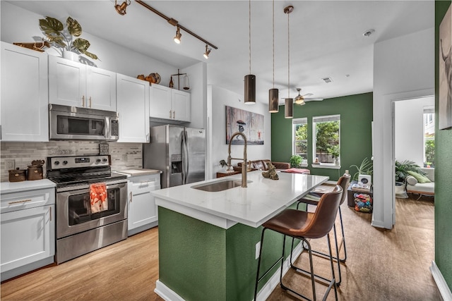 kitchen with appliances with stainless steel finishes, an island with sink, sink, white cabinets, and hanging light fixtures