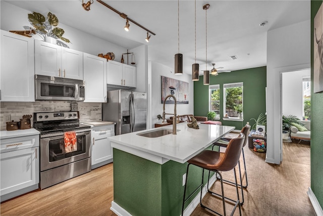kitchen featuring a sink, a kitchen island with sink, white cabinetry, decorative backsplash, and appliances with stainless steel finishes