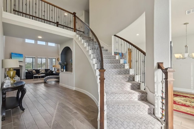 stairs with a towering ceiling, hardwood / wood-style floors, and a chandelier