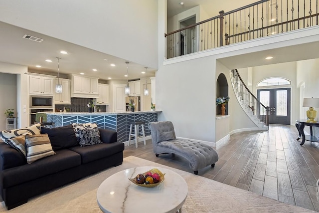 living room featuring french doors, a towering ceiling, and light wood-type flooring