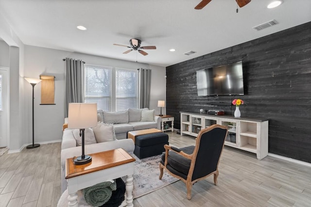 living room with wooden walls, ceiling fan, and light wood-type flooring