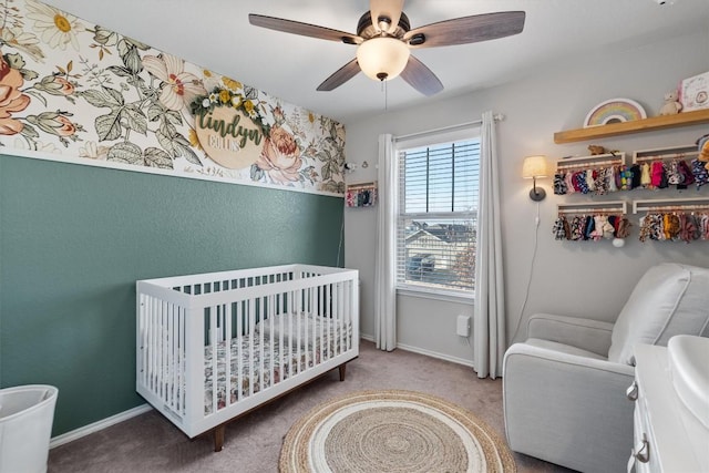 carpeted bedroom featuring a nursery area and ceiling fan