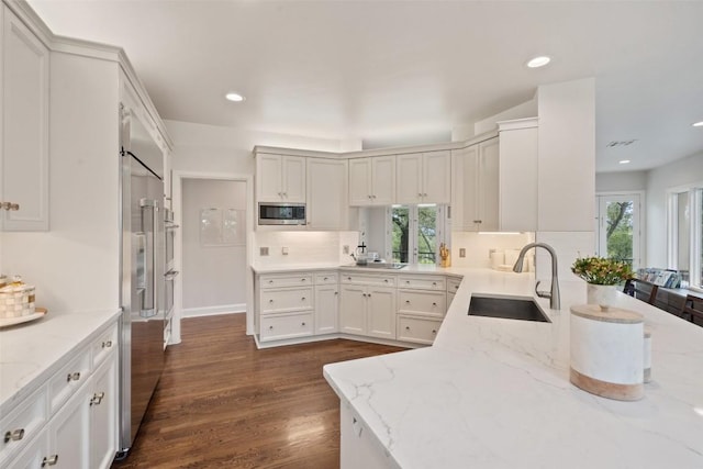 kitchen with stainless steel microwave, sink, decorative backsplash, light stone counters, and a healthy amount of sunlight