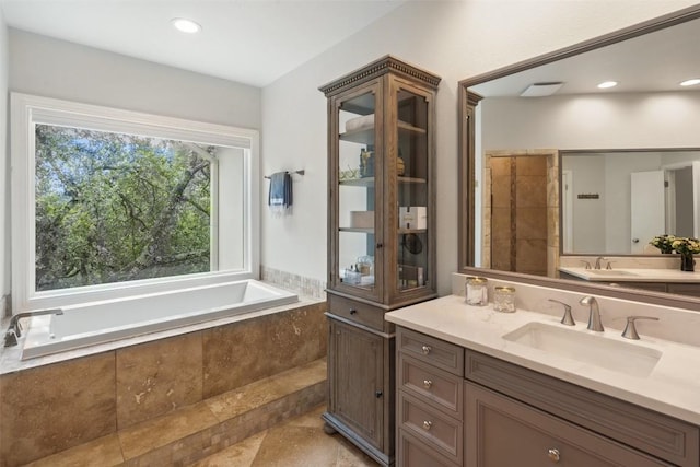 bathroom featuring a relaxing tiled tub and vanity