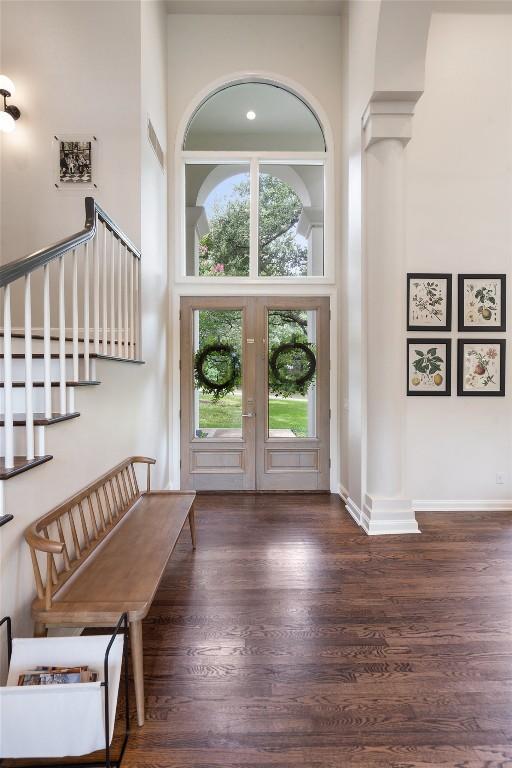 entryway featuring french doors, a towering ceiling, dark hardwood / wood-style flooring, and ornate columns