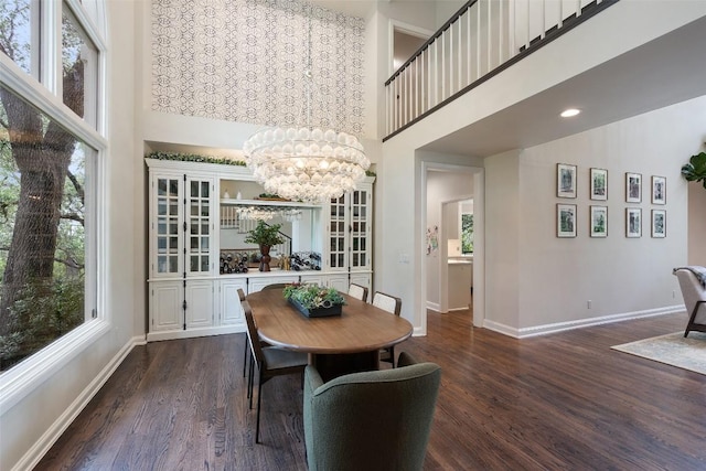 dining space with a towering ceiling, a wealth of natural light, dark hardwood / wood-style floors, and a chandelier