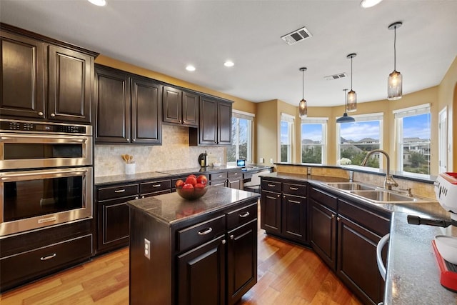 kitchen with a kitchen island, double oven, decorative light fixtures, sink, and dark brown cabinets