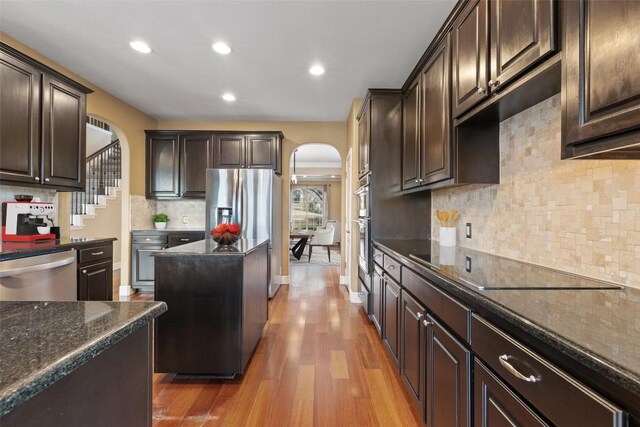 kitchen with dark stone countertops, stainless steel appliances, dark brown cabinetry, tasteful backsplash, and light wood-type flooring