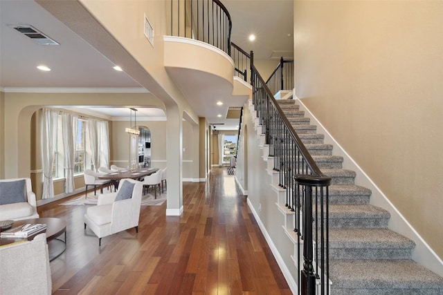 foyer with a towering ceiling, dark wood-type flooring, ornamental molding, and a healthy amount of sunlight