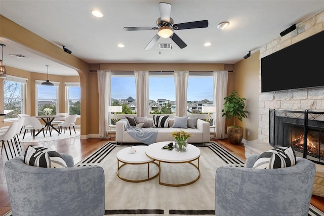 living room featuring a stone fireplace, light hardwood / wood-style flooring, and ceiling fan