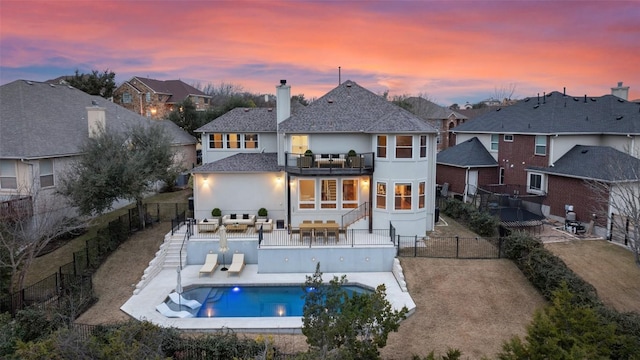 back house at dusk featuring a fenced in pool, a patio area, and a balcony