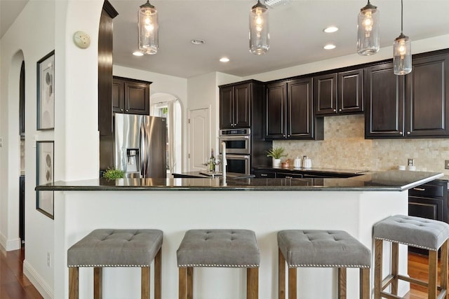 kitchen with tasteful backsplash, dark brown cabinets, a breakfast bar, arched walkways, and appliances with stainless steel finishes